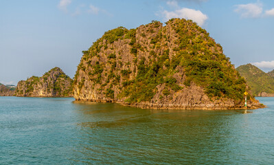 Naklejka premium A close up view from a cruise ship passing a Karst limestone islet in Ha Long Bay, Vietnam illuminated by the evening light
