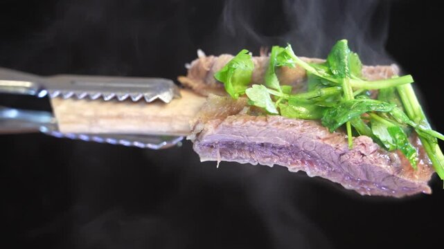 Tongs lifting hot galbitang topped with vegetables