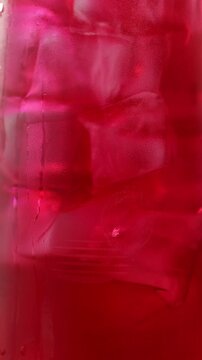 Close-up of ice cubes being stirred with a paper straw in a glass of healthy sparkling berry-flavored kombucha.