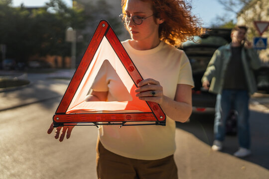 Woman holding warning triangle preparing roadside assistance after car breakdown