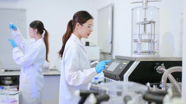 Two dedicated female scientists in lab coats working together, holding a clipboard and preparing liquid samples in test tubes during medical research