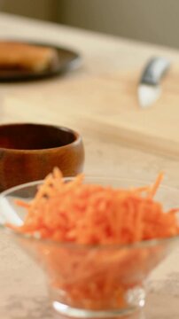 Vertical video: Sliding camera revealing glass bowl with shredded carrots on counter for meal prep