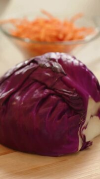 Vertical video: Pulling back camera from closeup on counter, showing half cabbage and carrot bowl