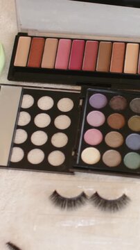 Vertical video: Tilting camera showing palettes and false lashes on towel, revealing amber bottles