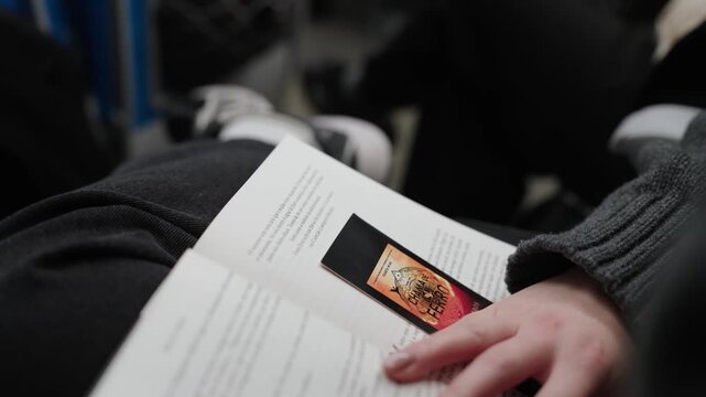 Hands holding open book closeup with pages turning and binding visible on Tokyo train