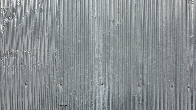 Dented and damaged corrugated metal wall. Gritty corrugated metal texture with visible dents and creases. Detailed view of a weathered corrugated steel fence. Authentic industrial background.