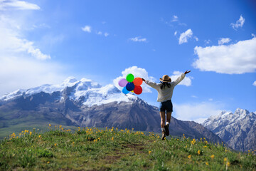Obraz premium Woman with colored balloons on sunset grassland mountain top