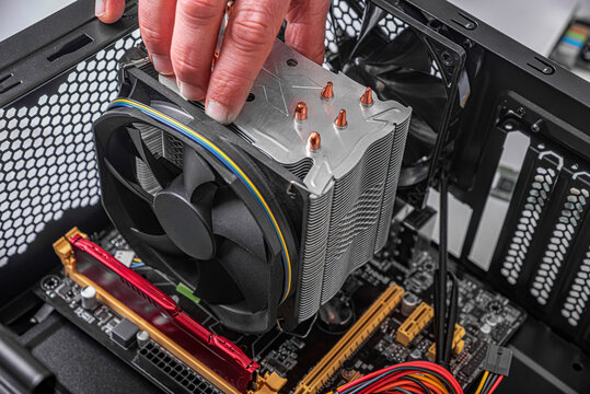 A technician's hand installs a large metal CPU cooler with a black fan onto a motherboard inside a computer chassis.