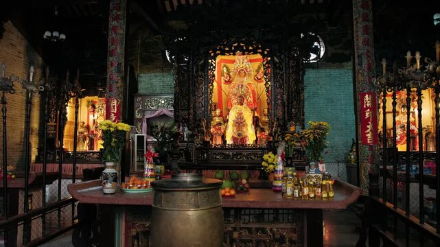 Interior of a traditional asian temple showing a richly decorated altar with a golden statue, offerings of fruit and burning candles, Ho Chi Minh city, Vietnam