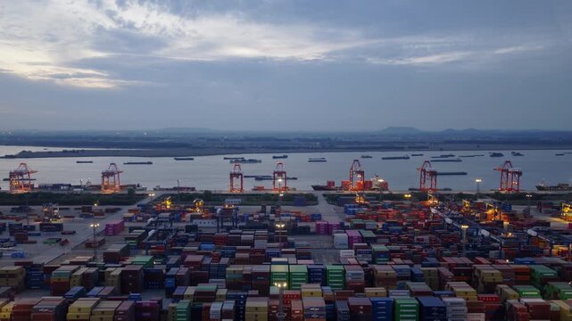 Aerial view over container stacks toward harbor and industrial port at dusk