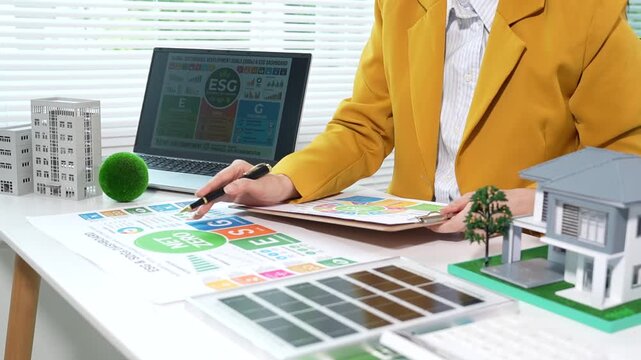 Businesswoman analyzing net zero and ESG sustainability reports with renewable energy model and eco-friendly office setup, focusing on green business strategy and carbon reduction.