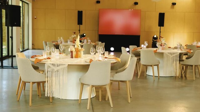 Wedding decor in boho style at banquet hall reception. Decorated round tables and chairs inside empty restaurant venue. Cinematic 4K slow motion footage of beautiful bohemian marriage celebration