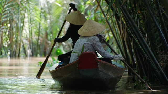 Vietnam women in a traditional boat on the mekong delta river through a lush tropical jungle in vietnam