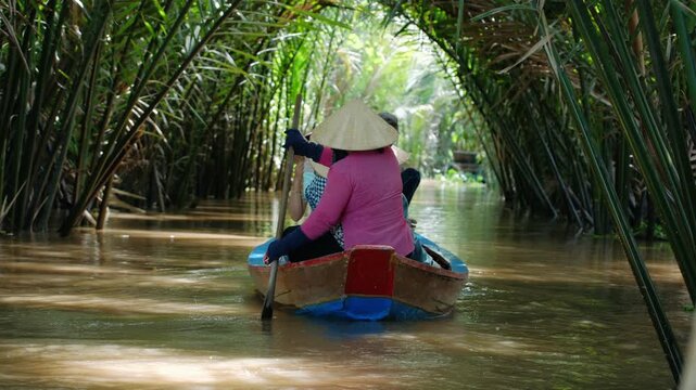 Vietnam woman in conical hat at boat with tourists on the mekong river delta through a lush jungle canal