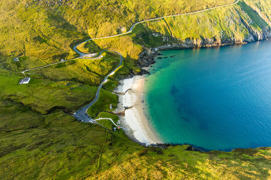 Keem Bay on Achill Island, County Mayo, Ireland, seen from above in warm evening light. This image shows the crescent beach, clear water, and steep green coastal slopes.