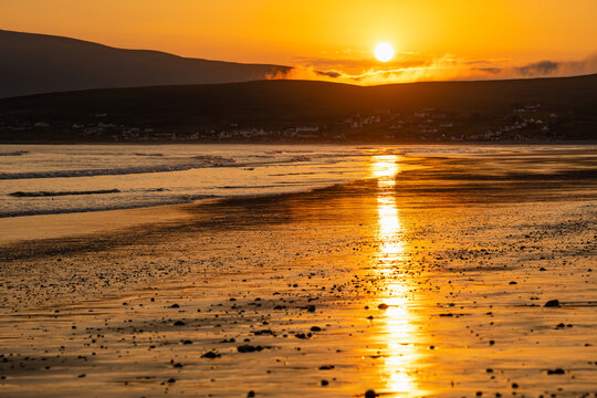 Golden sunset over Keem Beach on Achill Island, County Mayo, Ireland. Atlantic waves and wet sand reflect the evening sun beneath the hills of the Wild Atlantic Way.