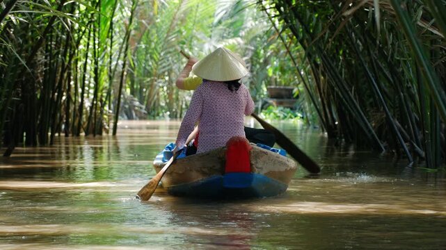 Women sailing at boat in mekong delta canal through tropical mangrove forest during tourist excursion, Vietnam