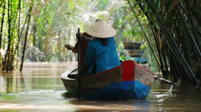 Vietnam woman in conical hat sailing at boat through mekong delta jungle canal, Vietnam