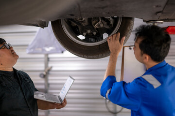 Obraz premium Auto mechanics team inspecting car undercarriage with laptop