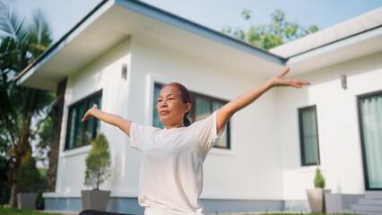 Woman stretches arms wide, smiling, outdoors. Modern house stands behind her, serene. Sunlight bathes her, peaceful, calm. Perfect for wellness, yoga, or relaxation themes © WARAPHON