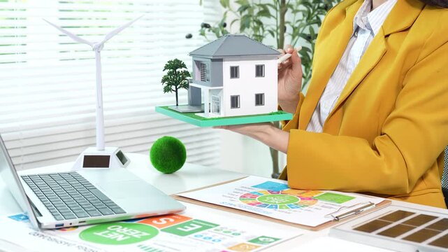 Businesswoman analyzing net zero and ESG sustainability reports with renewable energy model and eco-friendly office setup, focusing on green business strategy and carbon reduction.