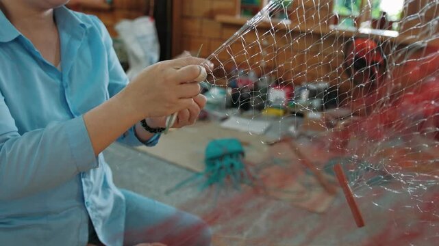 Vietnam woman weaving fishing net with handmade tools and nylon thread