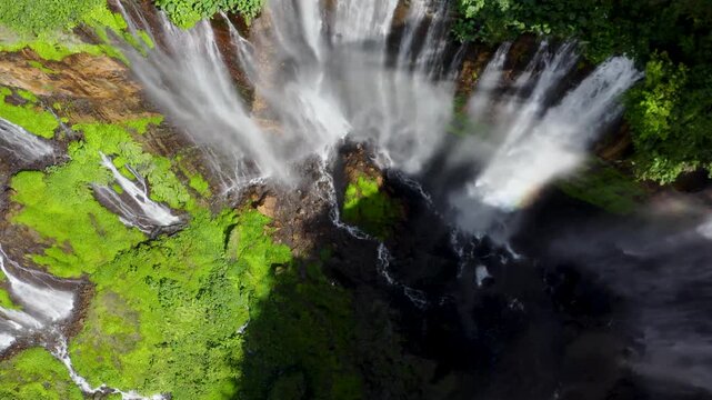 Aerial view of Grojogan Sewu Waterfall cascading down steep cliffs into a deep canyon surrounded by lush tropical vegetation in Kecamatan Pujon, Jawa Timur, Indonesia.