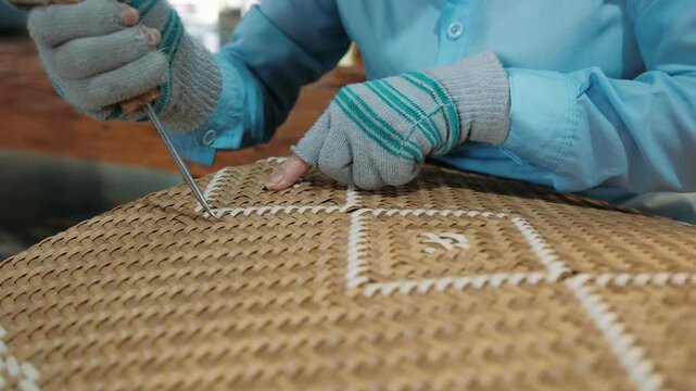 Artisan weaving a wicker chair seat in a furniture factory using natural rattan fibers and a handheld tool, Vietnam
