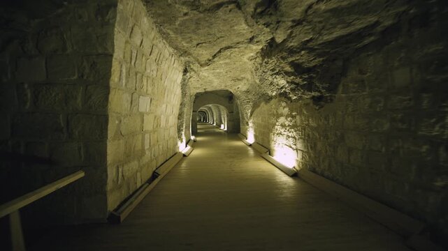 Dark rock-cut tunnel with successive stone arches and warm spotlights revealing massive black granite sarcophagus at end inside Serapeum of Saqqara, Egypt.