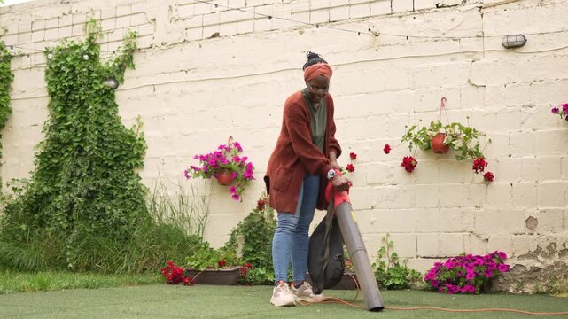 African american woman uses a leaf blower in her blooming garden