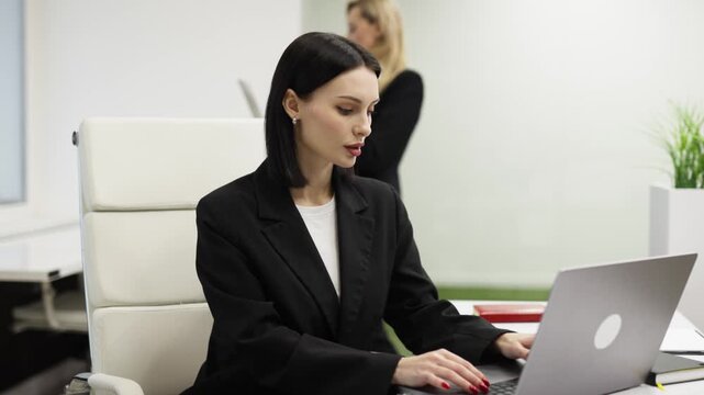 Office businesswoman typing on laptop and looking at camera in modern workspace. Concept productivity and modern corporate life.
