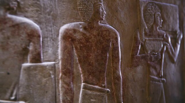 Close-up of detailed limestone relief carving inside tomb of Kagemni at Saqqara, Egypt, depicting ancient Egyptian male figures with tools, faint traces of original red pigment.
