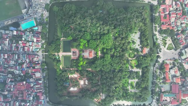 Vertical drone view of Son Tay Citadel enclosed by water moat and surrounded by dense greenery and city buildings.