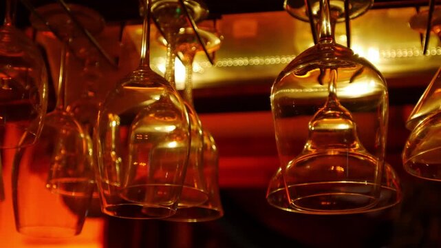 Wine glasses hanging upside down on rack above bar shelf with warm golden amber lighting elegant restaurant interior