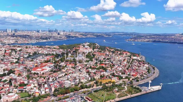 4K aerial view of Istanbul's historic peninsula with Hagia Sophia, Blue Mosque, Topkapı Palace, Sarayburnu and Bosphorus strait separating European from Asian side under summer clouds.