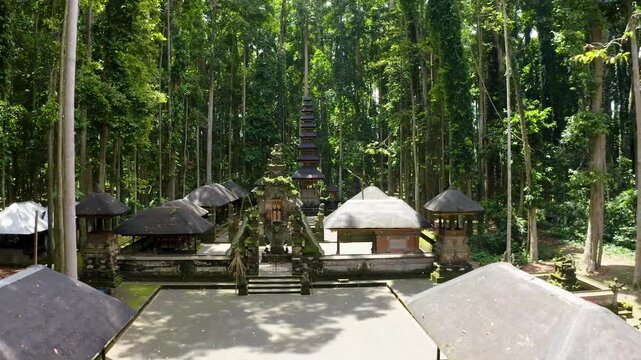Aerial view of a traditional Balinese Hindu temple with a multi-tiered Meru tower surrounded by a lush green forest in Bali, Indonesia.