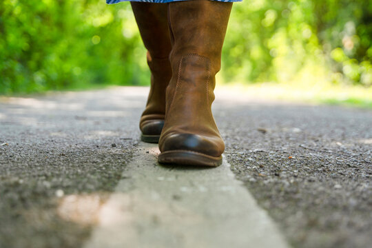 Walking on a path in brown boots through green trees in a sunny outdoor area during the daytime