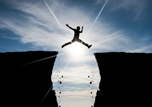 Silhouette of a Man Jumping Over a Gap Between Two Cliffs Against a Br