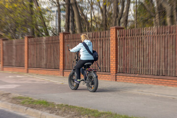 Fototapeta premium Woman riding electric bicycle on bike path. Active person travels through city on bike.