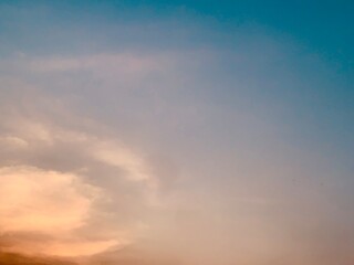 Obraz premium Soft blue sky with pastel clouds and warm sunset glow, minimal dreamy atmosphere captured from below with smooth gradients and gentle light, ideal for background, calm and nature themes.