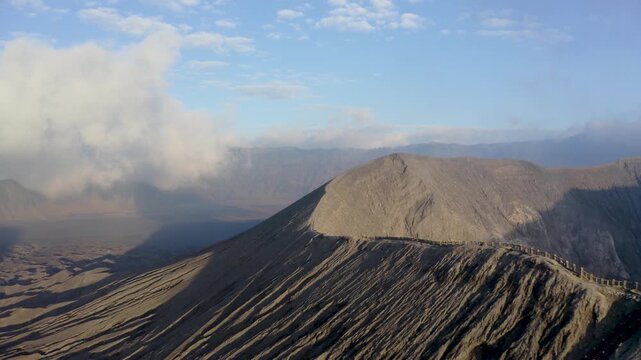 Aerial view of Mount Bromo crater ridge with steep volcanic slopes under a blue sky with clouds Tosari, East Java, Indonesia.