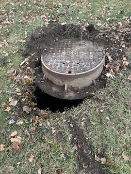 Open manhole cover in grassy park area with exposed underground utility access
