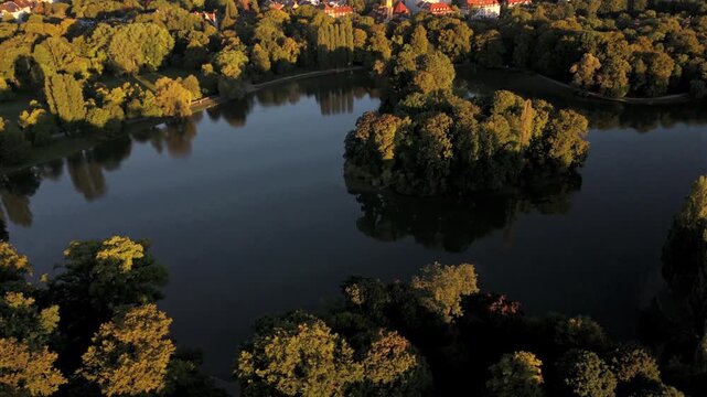 Air view over Kleinhesseloher See, artificial lake in the English Garden, Munich, Bavaria. Surrounded by trees, meadows, beer gardens and cultural landmarks. German urban nature site