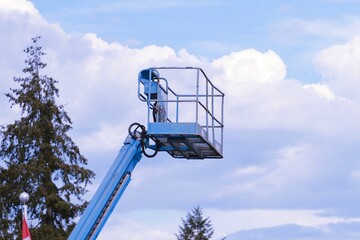 Blue cherry picker boom lift bucket platform against cloudy sky © Diane