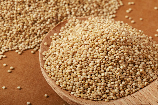 Close-up of quinoa seeds (Chenopodium quinoa) in wooden spoon on rustic brown surface, selective focus