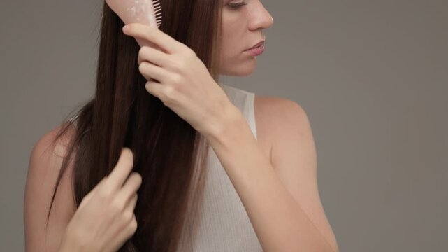 A woman with dark brown hair combing it with a comb