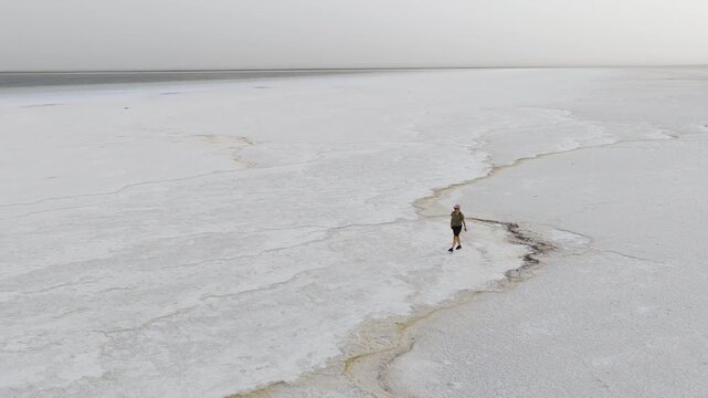Aerial view of a person walking across the vast white salt crust patterns of the Danakil Desert under a hazy sky in Dalol, Afar, Ethiopia.