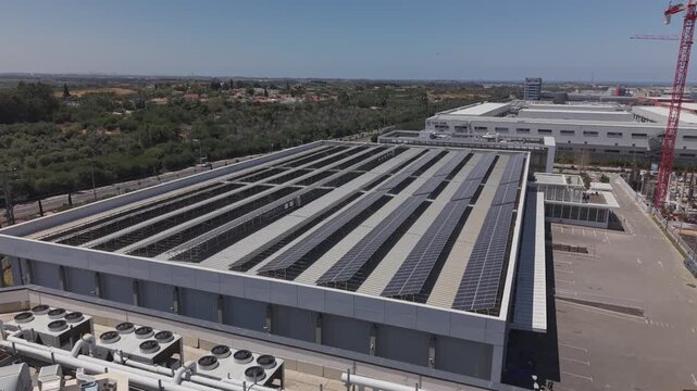 Aerial view of warehouse rooftop with solar panels, boilers and ventilation systems beside construction crane and orchards in Israel
