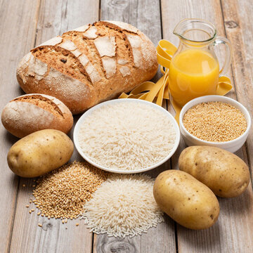 Assorted Carbohydrate Rich Foods Including Bread, Rice, Pasta, and Potatoes on Wooden Surface
