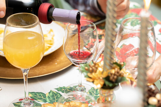 dettagli di una scena durante un pranzo o cena natalizio italiano, vino rosso che viene versato da una bottiglia dentro ad un calice, tavolo apparecchiato e con decorazioni di natale